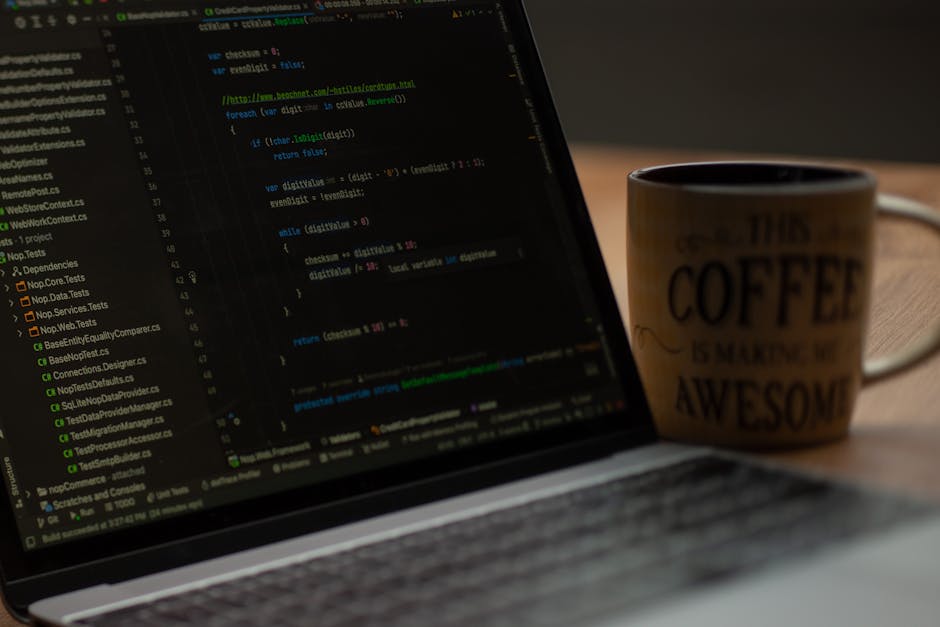 A close-up view of a desk surface in an office environment, featuring two black computer monitors, one displaying a code editor with colorful syntax highlighting, and the other turned off. The worksta
